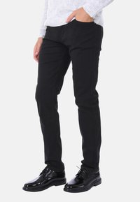 Pantaloni neri a taglio slim in denim, dotati di quattro tasche. Abbinati a scarpe eleganti nere lucide e a un maglione grigio chiaro con trama.