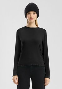 Zwarte lange mouwen top met een ronde halslijn, franjes aan de zoom en een zachte, gladde stof, gecombineerd met een zwarte gebreide beanie.