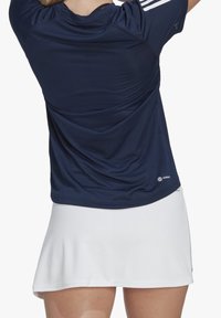 Marinblå atletisk tröja med strukturerad yta, korta ärmar och tre vita ränder på axlarna; matchad med en vit, fluffig kjol.