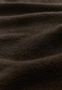 Ciemnobrązowy materiał o miękkiej, teksturowanej powierzchni, z delikatnymi wzorami i łagodnymi falami, odbijając światło w różnych odcieniach.