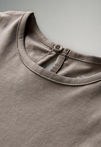 Zbliżenie na neckline beżowej bawełnianej koszuli z okrągłym kołnierzykiem i małym zapięciem na guziczek z tyłu.