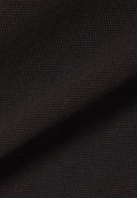 Close-up van zwart gestructureerd stof met een fijn gaaspatroon en een lichte diagonale plooi die schaduwen en diepte creëert.