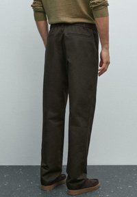 Pantalons en coton mélangé vert foncé avec une coupe décontractée, taille élastique et poches latérales, vus de l'arrière. Texture lisse avec un minimalisme dans les détails.