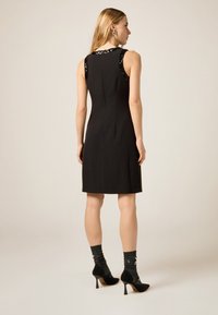 Sort ærmeløs kjole med palietter på skuldrene, tætsiddende design, knælængde, kombineret med teksturerede sorte sokker og sko med hæl.