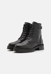 Botas de cuero negro hasta el tobillo con punta redonda, cordones en la parte delantera, costuras laterales y un tacón bajo tipo bloque. Incluyen un detalle de hebilla plateada.