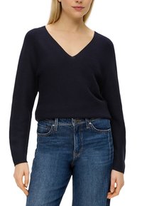 Marineblå V-ringad stickad tröja med långa ärmar, kombinerad med blå denimjeans. Tyget har en ribbad textur och en avslappnad passform.