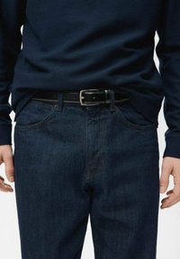 Navy long-sleeve shirt paired with dark wash denim jeans. Black leather belt with silver buckle. Visible front pockets and stitching detail.