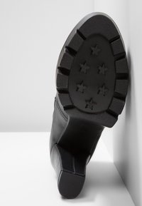 Stivaletto in pelle nera con robusto tacco a blocco. La suola presenta un motivo a stelle ed è testurizzata per una migliore aderenza, garantendo durata e supporto.