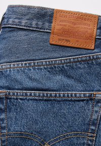 Jeans de mezclilla azul con costuras naranjas y un parche de cuero marrón de Levi Strauss & Co. en la cinturilla, encima del bolsillo trasero.