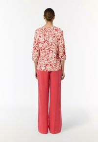 Czerwona i biała bluzka w wzory z rękawami o długości trzech czwartych, zestawiona z szerokimi różowymi spodniami, gładka tekstura i luźny krój.