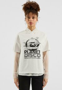 Witte t-shirt met korte mouwen met een zwart geprint grafisch ontwerp van een discobal en de tekst "PLANET DISCO" in vette letters. Transparante accenten op de mouwen.