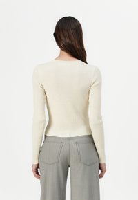 Maglione crema a coste con maniche lunghe e scollatura a girocollo. Abbinato a pantaloni grigi chiari a vita alta con tasche posteriori.