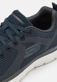 Granatowe siatkowe sneakersy z teksturowanym wzorem, charakterystycznym logo, wzmocnionymi sznurówkami, wyściełanym kołnierzem i lekką białą podeszwą dla komfortu.