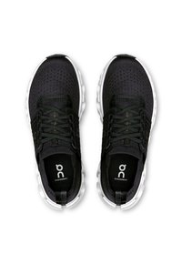 Chaussures de sport noires avec une tige en maille respirante, lacets noirs et semelle blanche. Comprend un logo sur la semelle intérieure et des détails au niveau du talon.
