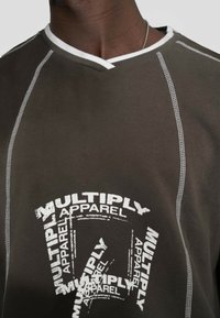 Hnedá mikina s bielym prešívaním a výstrihom do V. Obsahuje opakujúcu sa grafiku s nápisom "MULTIPLY APPAREL" v rôznych veľkostiach.