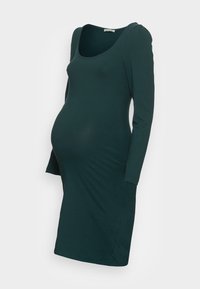 Mörkgrön, långärmad gravidklänning med rundad halsringning och figurnära silhuett designad för att rymma en babymage.