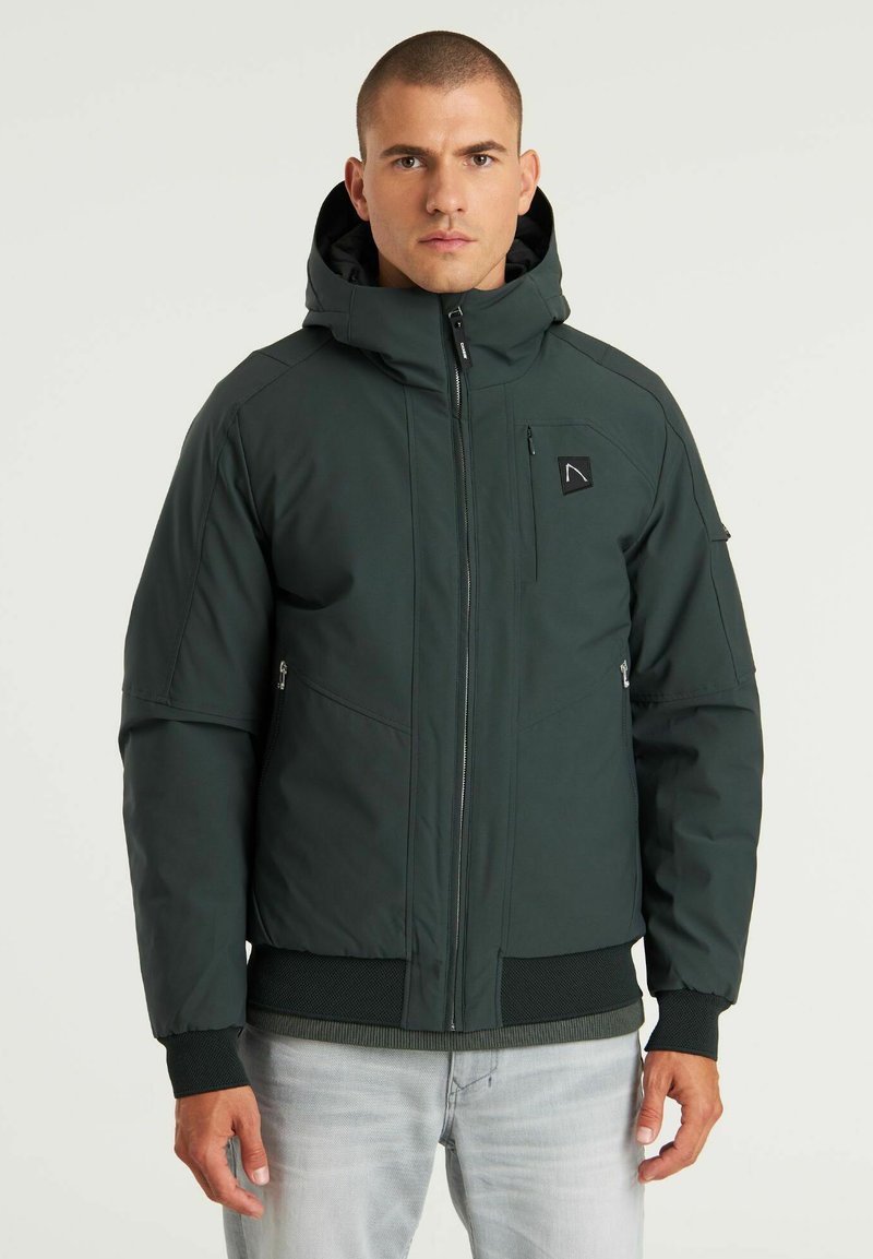 Chaqueta aislante verde oscuro con capucha, que cuenta con una cremallera frontal, bolsillos laterales, puños acanalados y un logo en el pecho. Textura suave.