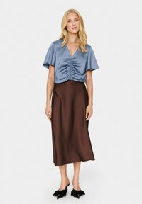 Kék selyem cropped top, elöl gathered részlettel, egy laza barna selyem midi szoknyával és fekete hegyes orrú szandálokkal párosítva.