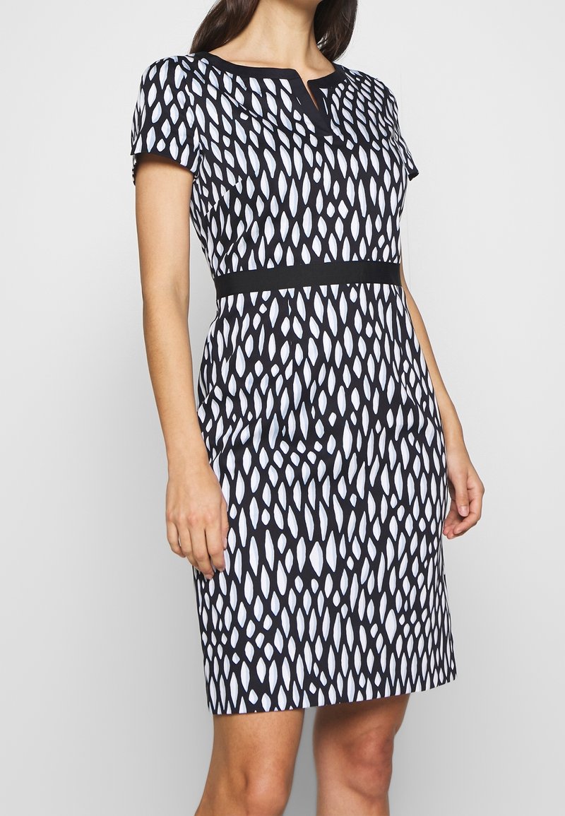 Robe à motifs en noir et blanc avec des manches courtes, un décolleté en V et une taille noire. Le design présente des formes allongées sur un fond clair.