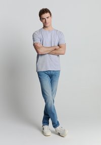 Grijze t-shirt met korte mouwen, lichtblauwe jeans en witte sneakers. De t-shirt heeft een ronde hals; de jeans zijn rechtafgesneden met een vervaagd uiterlijk.