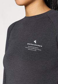 Tummanharmaa pitkähihaisuus, joka on valmistettu Tencel-, villa- ja elastaaniseoksesta. Sisältää valkoisen painetun logon ja tekstin rinnassa sekä raglan-hihat.