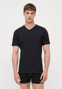 T-shirt noir en coton à col en V avec des manches courtes et une coupe ajustée. Texture lisse, détails de couture minimaux, porté avec des slips noirs.