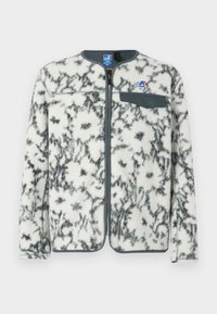 Fleecejakke med lynlås fortil, med en hvid bund og sorte marmoreringer, grå detaljer og en brystlomme med trykknaplukning.