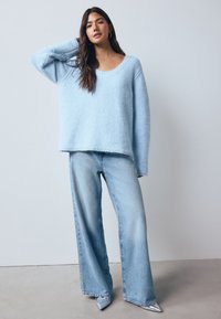 Light blue fluffy sweater with a wide scoop neckline, paired with light blue wide-leg jeans and pointed silver shoes. Simple, soft textures.