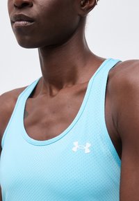 Κοντινό πλάνο ενός ατόμου που φοράει ανοιχτό μπλε αμάνικο αθλητικό μπλουζάκι με λευκό λογότυπο Under Armour στο στήθος.