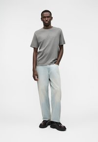 Γκρι κοντομάνικη μπλούζα με διακριτικό λογότυπο, συνδυασμένη με ανοιχτό μπλε φαρδιά τζιν και μαύρα chunky αθλητικά παπούτσια. Λείο ύφασμα.