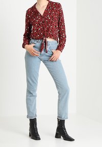 Blouse courte à imprimé léopard rouge avec un nœud à l'avant, associée à un jean taille haute bleu clair et des bottines noires à talons.