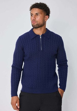 Pull en maille bleu marine avec un motif torsadé, manches longues et col avec fermeture éclair à moitié. Texture douce et coupe ajustée.
