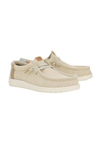 Scarpe in tela beige chiaro con una finitura testurizzata e suola in gomma bianca. Presentano lacci elastici e dettagli intrecciati in contrasto.