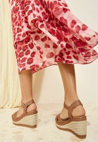 Bruine gevlochten wedge sandalen met een verhoogd geweven jute platform. Het bandjesdesign laat huid zien en heeft een ronde gesp.