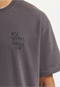 Pelēks kokvilnas T-krekls ar īsām piedurknēm un apaļu apkakli. Uz priekšpusi ir melna uzdruka "ROC STARS NEVER DIE".