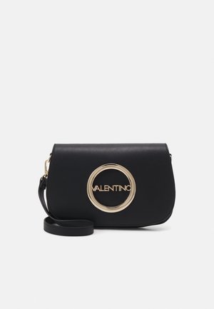 Bolso de piel negra tipo bandolera con forma curvada, que presenta un acento de logo circular dorado y una correa desmontable. Textura suave, diseño minimalista.