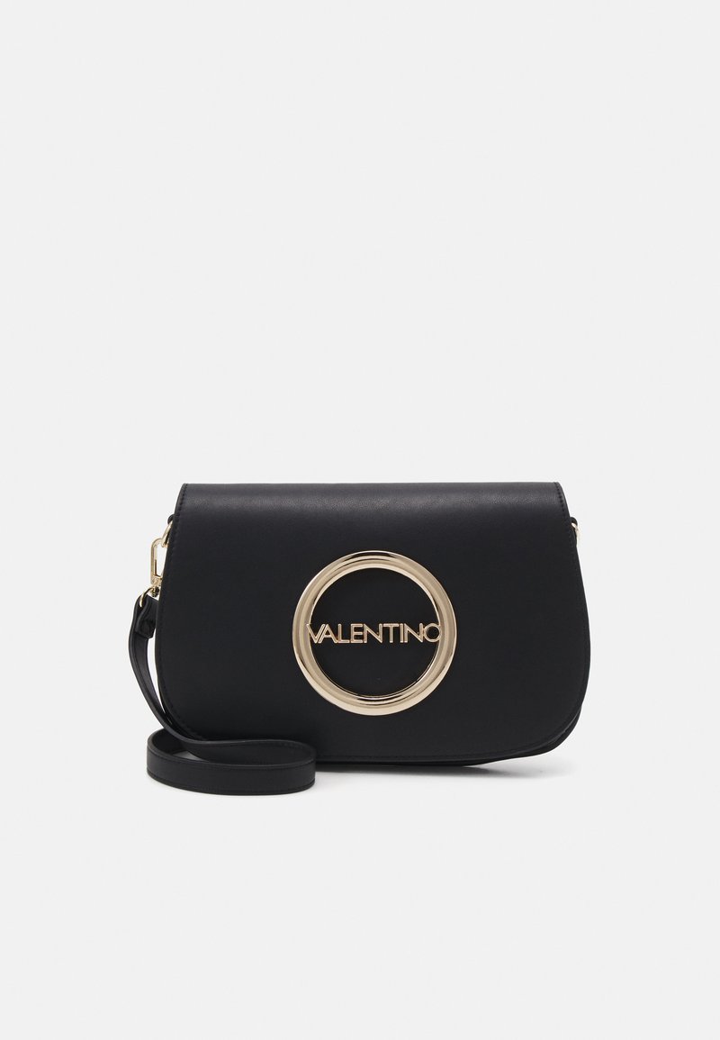 Bolso de piel negra tipo bandolera con forma curvada, que presenta un acento de logo circular dorado y una correa desmontable. Textura suave, diseño minimalista.