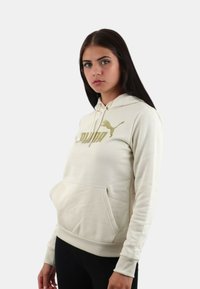 Felpa color crema con tasca a canguro, polsini a costine e design del logo dorato sul petto. Tessuto morbido e vestibilità casual.