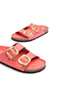 Sandalias de dos correas en color coral rosa, hechas de un material de goma suave, con grandes hebillas doradas, que cuentan con una plantilla de corcho y una suela negra.