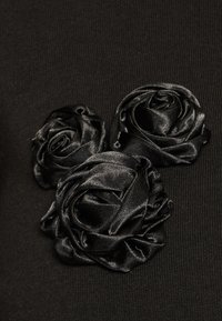 Black top featuring three black satin rose appliqués on a textured fabric background. The design emphasizes a smooth, rich texture and floral detail.