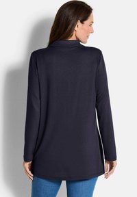 Tunic a maniche lunghe in tessuto blu navy, con colletto, fessure laterali e una vestibilità comoda. Abbinata a pantaloni di denim, mostrando una texture morbida.