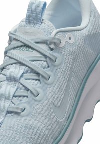 Sapatilha atlética azul clara com parte superior texturizada, ilhoses redondos e alça; apresenta um swoosh branco e uma sola de borracha ondulada.