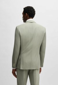 Giacca di costume verde chiaro con una vestibilità sartoriale, apertura centrale sul retro e polsini bottonati. Tessuto testurizzato con una lucentezza sottile.