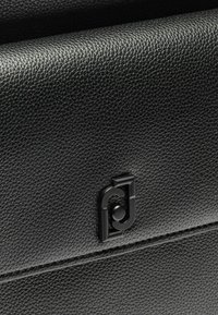 Borsa in pelle nera testurizzata con un logo in rilievo liscio di colore contrastante, che dimostra un design elegante e minimalista.