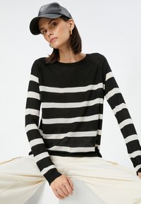 Sort og hvid stribet langærmet sweater med rund halsudskæring og ribbede manchetter, båret med cremefarvede cargo-bukser og en sort læderkasket.