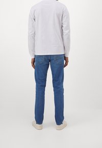 Modré džíny s úzkým střihem a zadními kapsami, spojené s bílou košilí s dlouhým rukávem. Vyznačují se jednoduchým, čistým designem.