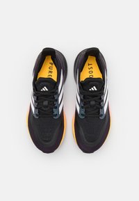 Des chaussures de sport noires présentent trois rayures blanches, une tige en maille et synthétique, une semelle intérieure jaune et une semelle multicolore avec des accents orange et violet.