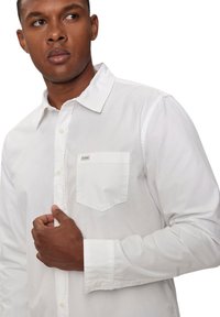 Camicia bianca in cotone con bottoni, caratterizzata da una tasca sul petto con logo, maniche lunghe e collo classico.