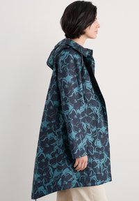 Gevoerde jas in donker marineblauw met een teal bloemenpatroon, beschikt over een ontspannen pasvorm, knoopsluiting en zijzakken. Zachte stoftextuur.