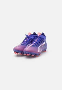 Botas de fútbol con un diseño degradado en púrpura y rosa, que cuentan con un collar tipo calcetín, superficie texturizada y tacos multicolores.
